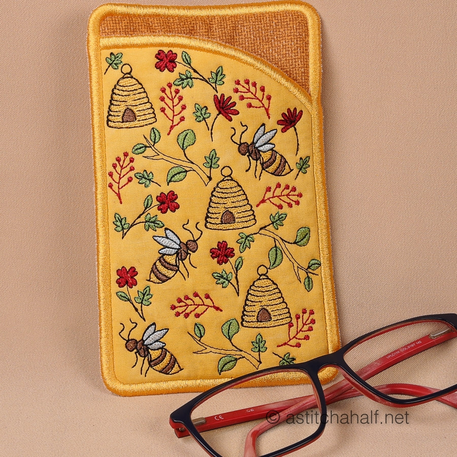 Two embroidered glasses cases with bee and honeycomb patterns on a beige background, with a pair of glasses in front.