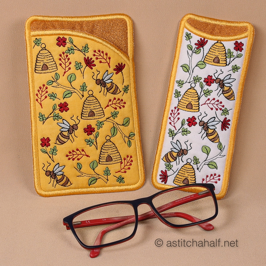 Two embroidered glasses cases with bee and honeycomb patterns on a beige background, with a pair of glasses in front.