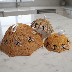 Three decorative umbrellas with bee patterns on a textured white background
