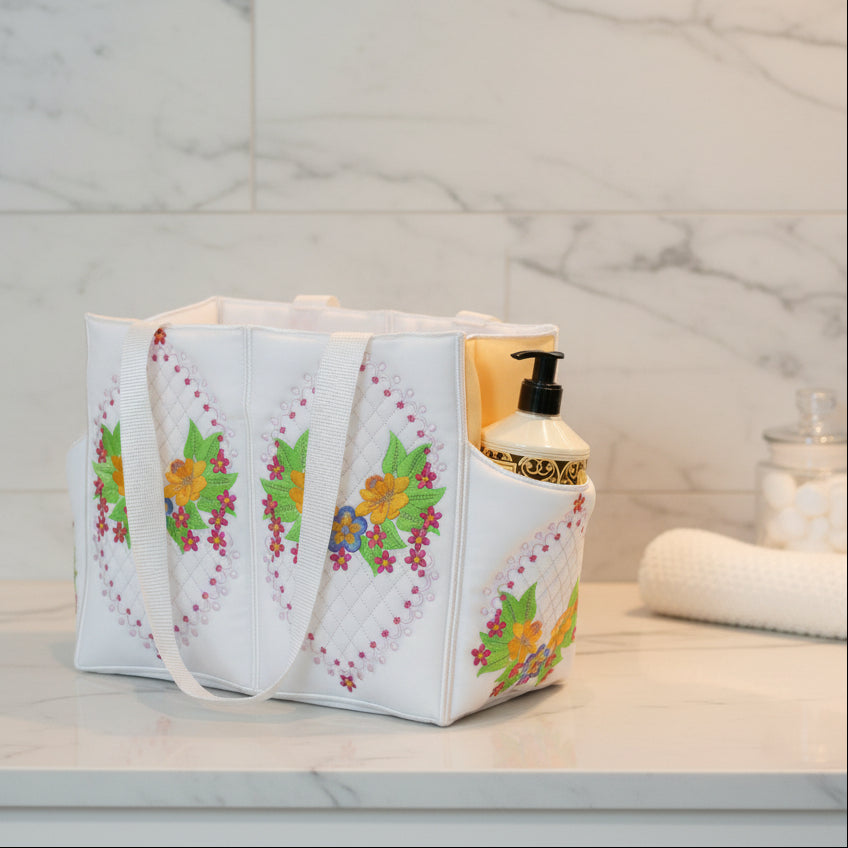 White tote bag with floral embroidery containing a bottle of lotion on a beige surface.