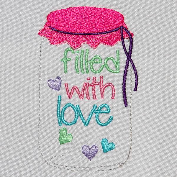 White towel with 'Filled with Love' text on a wooden surface with flowers and jam jar.