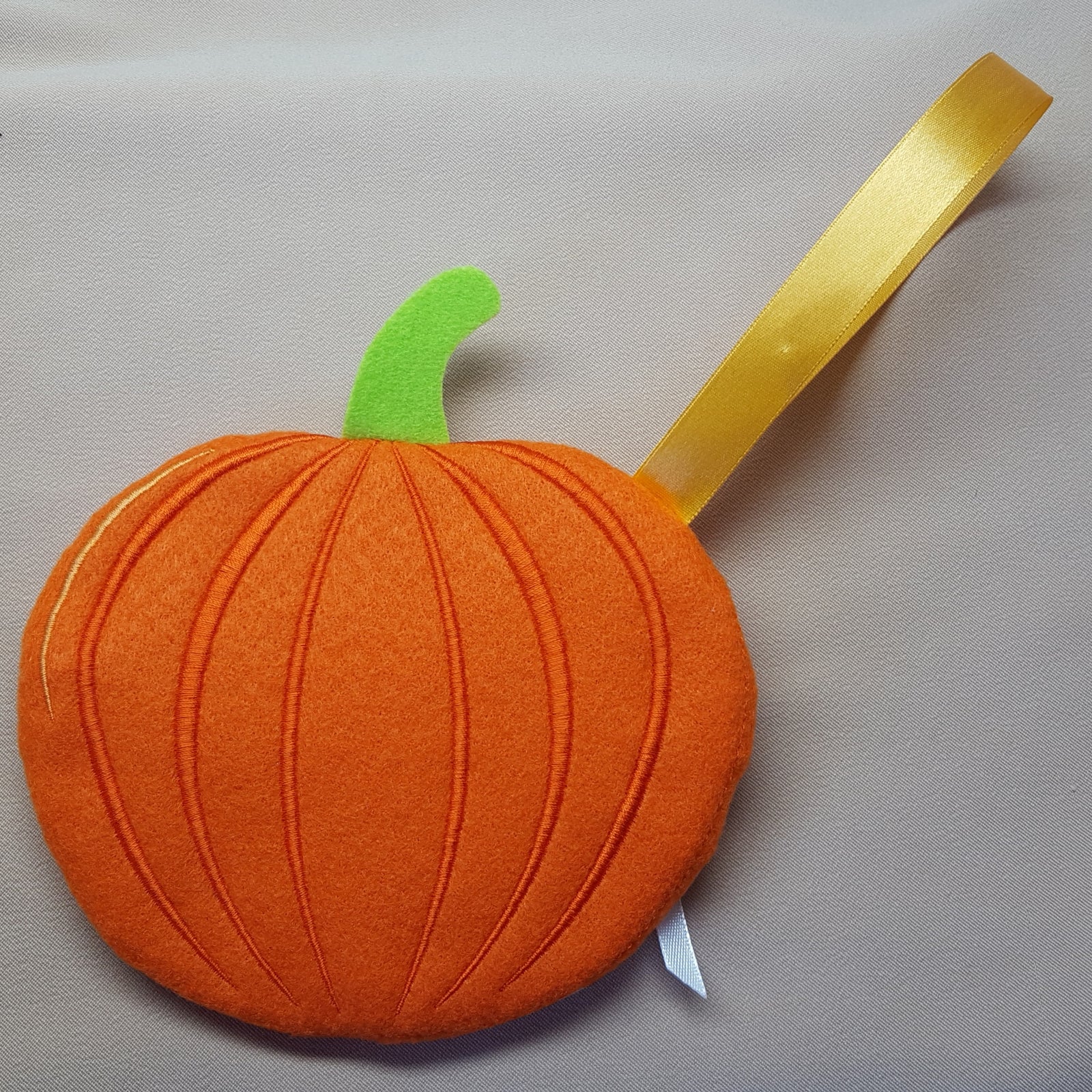 Orange felt pumpkin with a green stem and yellow leaf on a gray background
