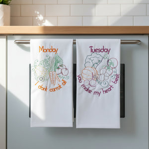 Two embroidered towels with vegetable-themed designs and text on a beige background.