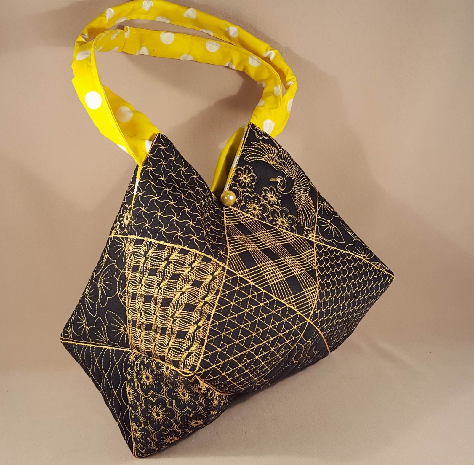 Black handbag with gold embroidery and yellow polka dot strap on a beige background