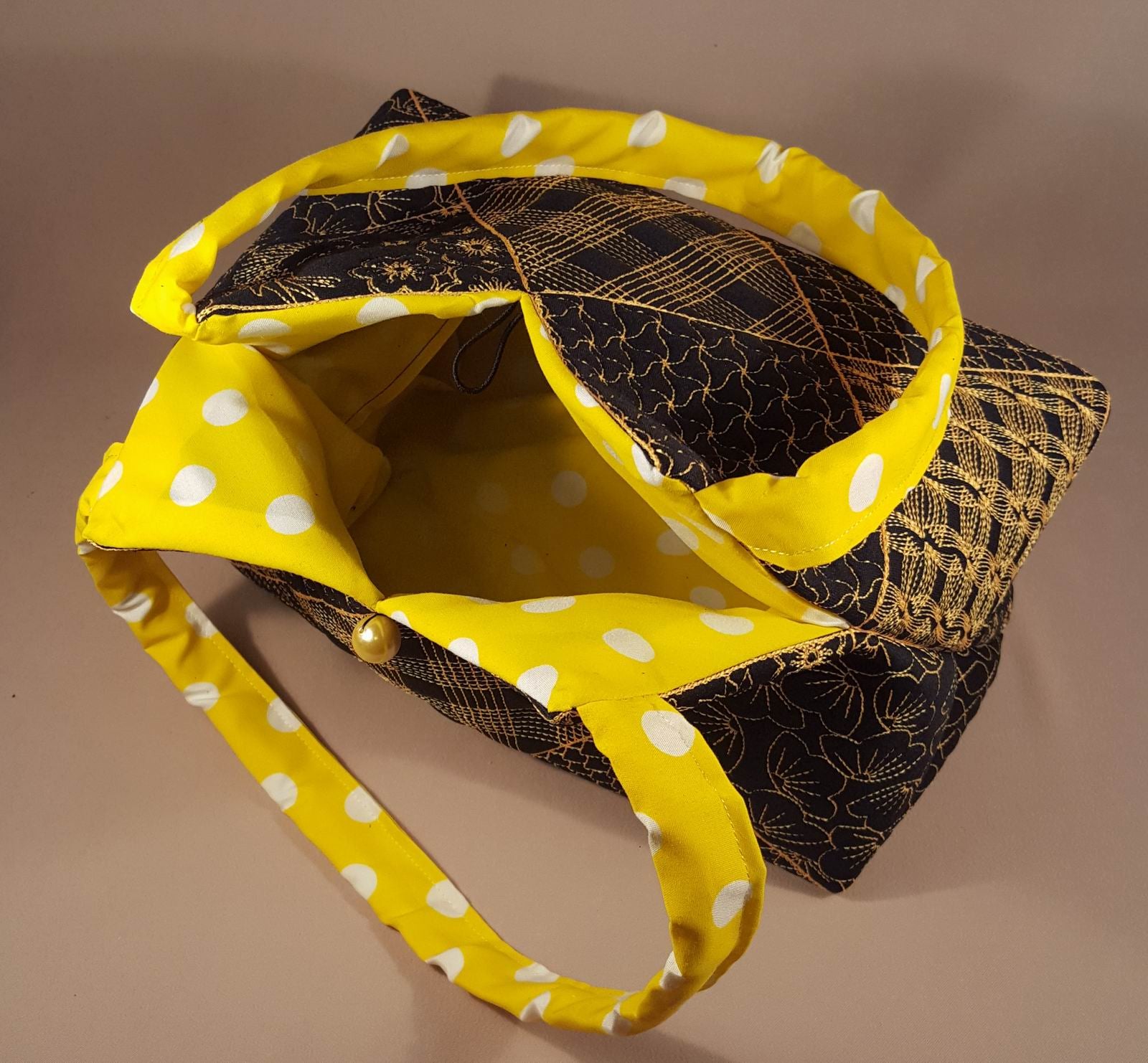 Black handbag with gold embroidery and yellow polka dot strap on a beige background