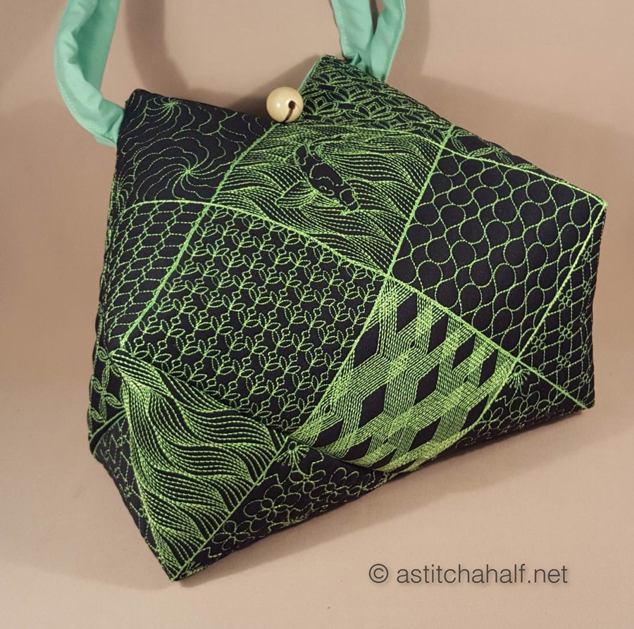 Green and black patterned handbag with a gold button on a beige background
