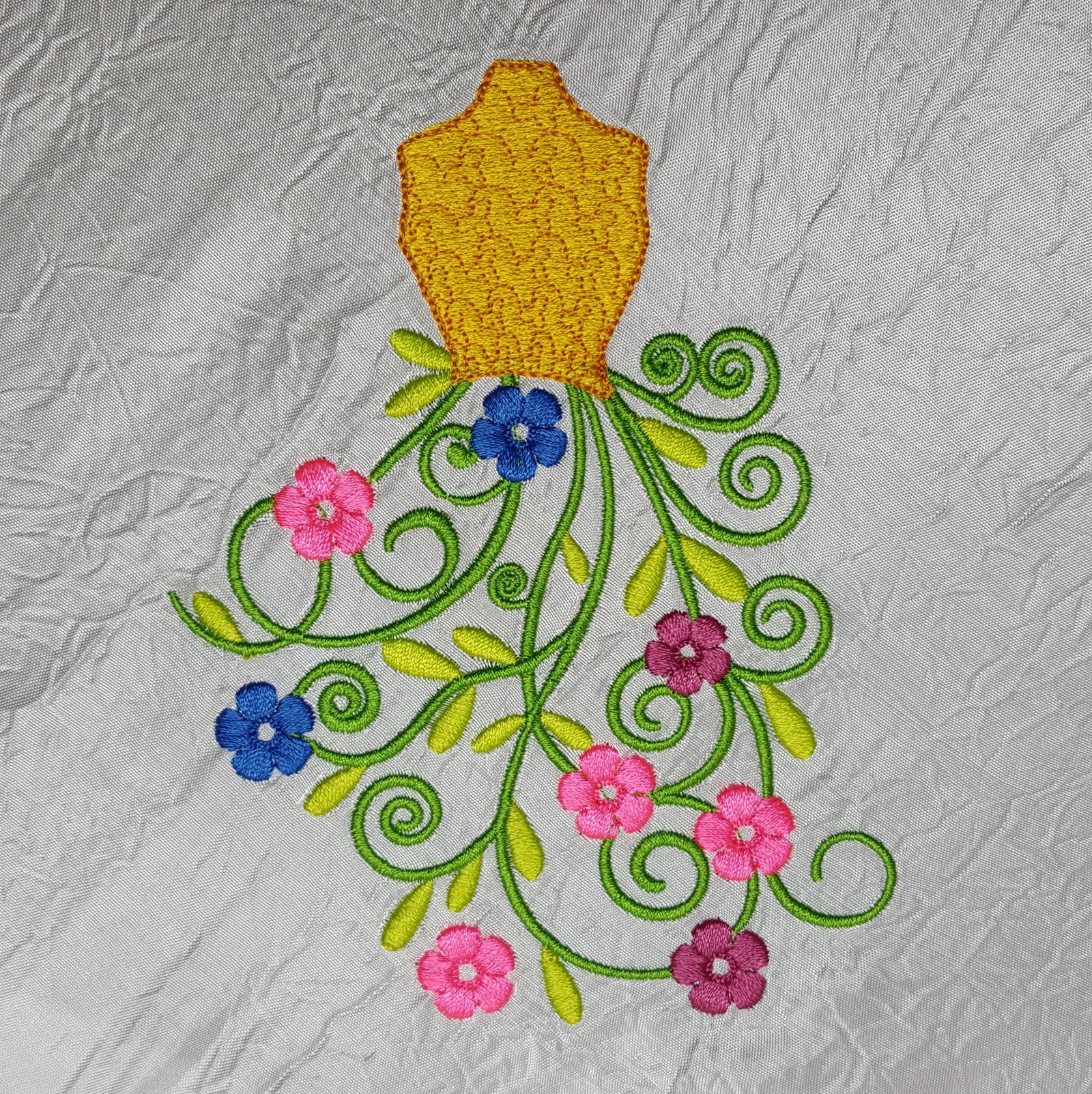 White notebook with embroidered dress design on a wooden surface with sewing materials.