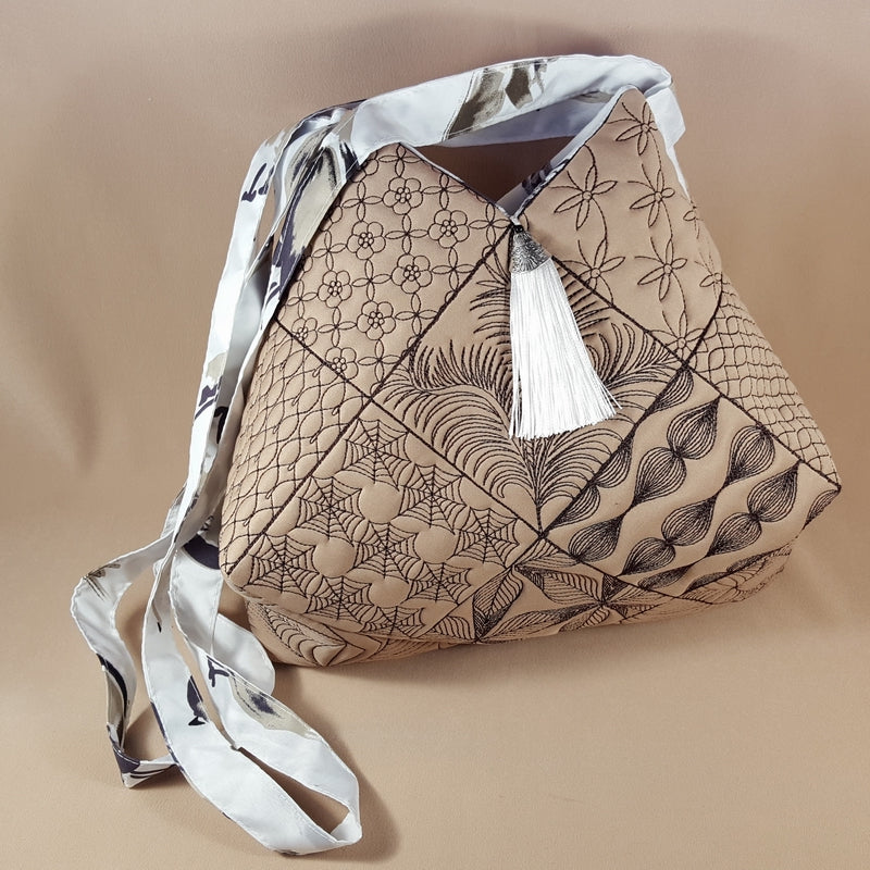 Beige handbag with floral patterns and a white tassel on a beige background