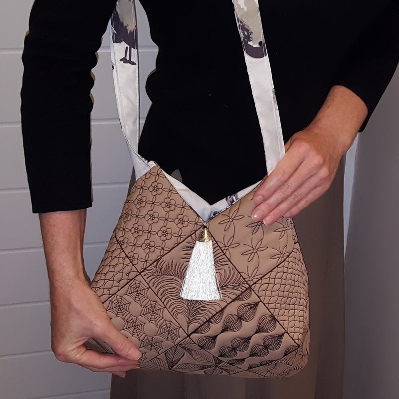 Beige handbag with floral patterns and a white tassel on a beige background