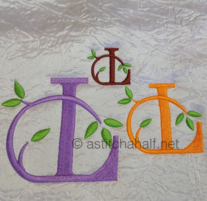 Embroidered letters 'L' in purple and orange with green leaves on a textured fabric background.