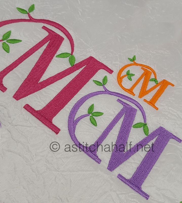 Embroidered letters 'MOM' in pink, orange, and purple with green leaves on a textured white background.