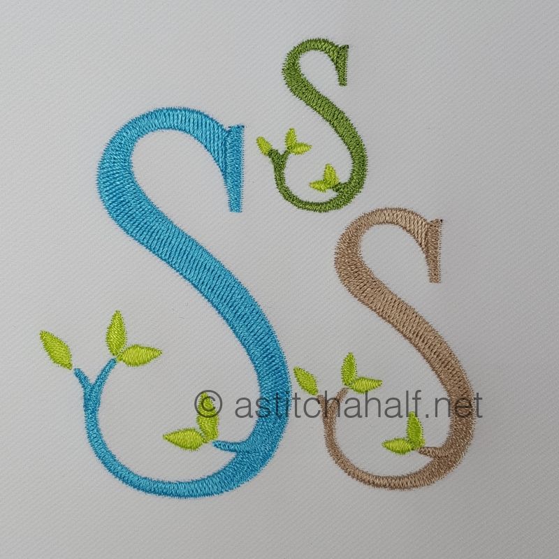 Embroidered letters 'A' in various colors with green leaves on a textured fabric background.