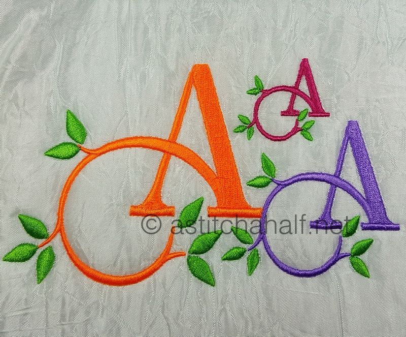 Embroidered letters 'A' in various colors with green leaves on a textured fabric background.