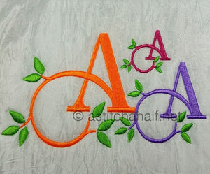 Embroidered letters 'A' in various colors with green leaves on a textured fabric background.