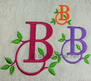 Embroidered letters 'B' in various colors with green leaves on a textured fabric background.