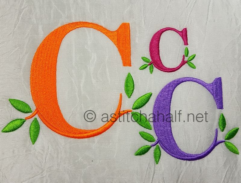 Embroidered letters 'C' in orange, pink, and purple with green leaves on a textured gray background.