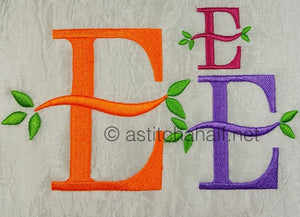 Embroidered letters 'E' in various colors with green leaves on a textured fabric background.