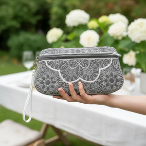 Person holding a gray floral-patterned clutch bag outdoors with white flowers in the background