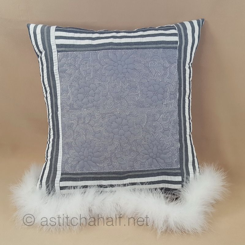 Beige sofa with a textured gray pillow and knitted blanket, next to a small table with a plant.