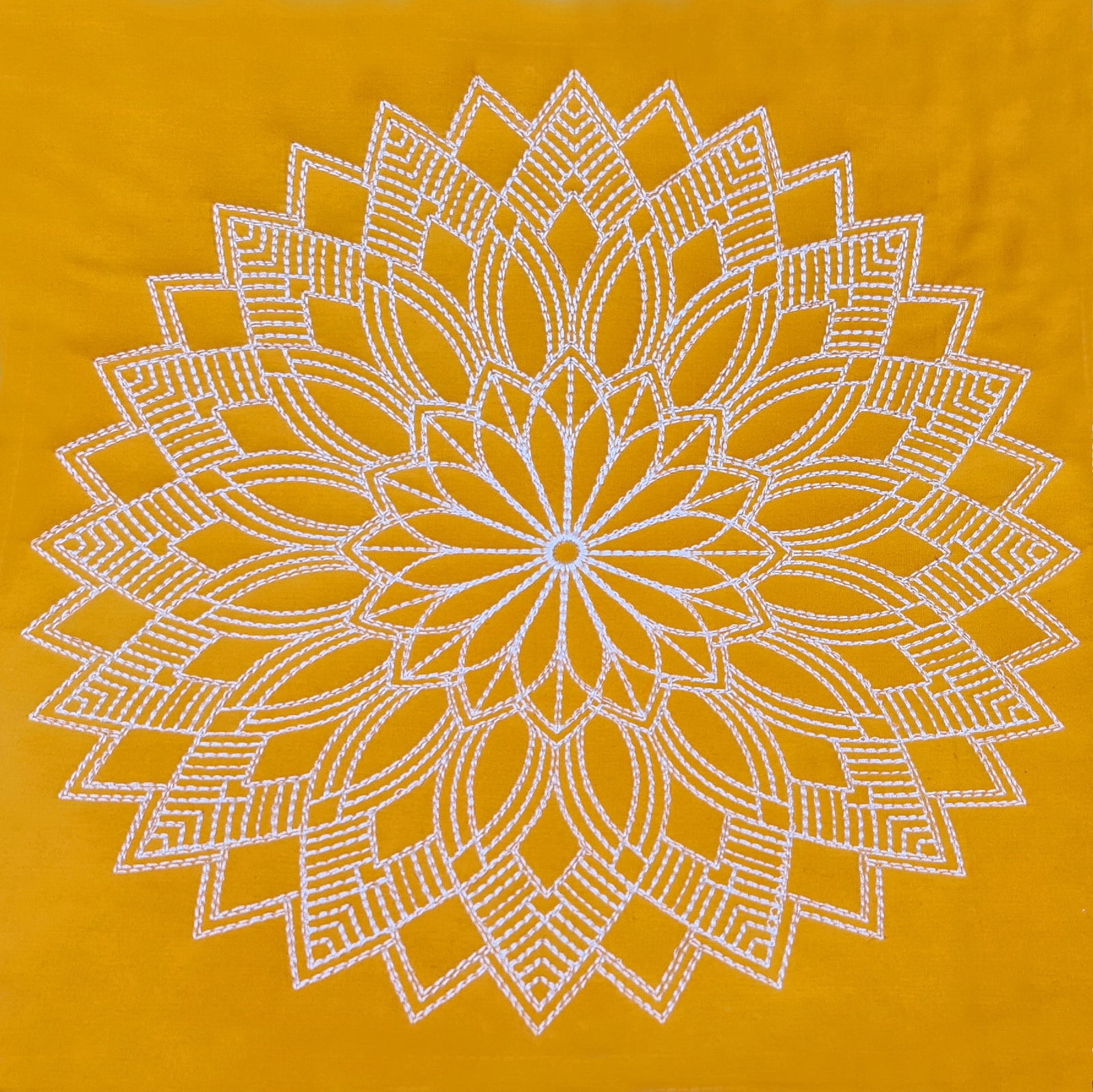 Yellow floral-patterned blanket on a bed with a wooden nightstand and potted plant.