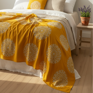 Yellow floral-patterned blanket on a bed with a wooden nightstand and potted plant.