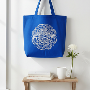 Blue tote bag with 'BE KIND' design hanging on a hook against a white wall.
