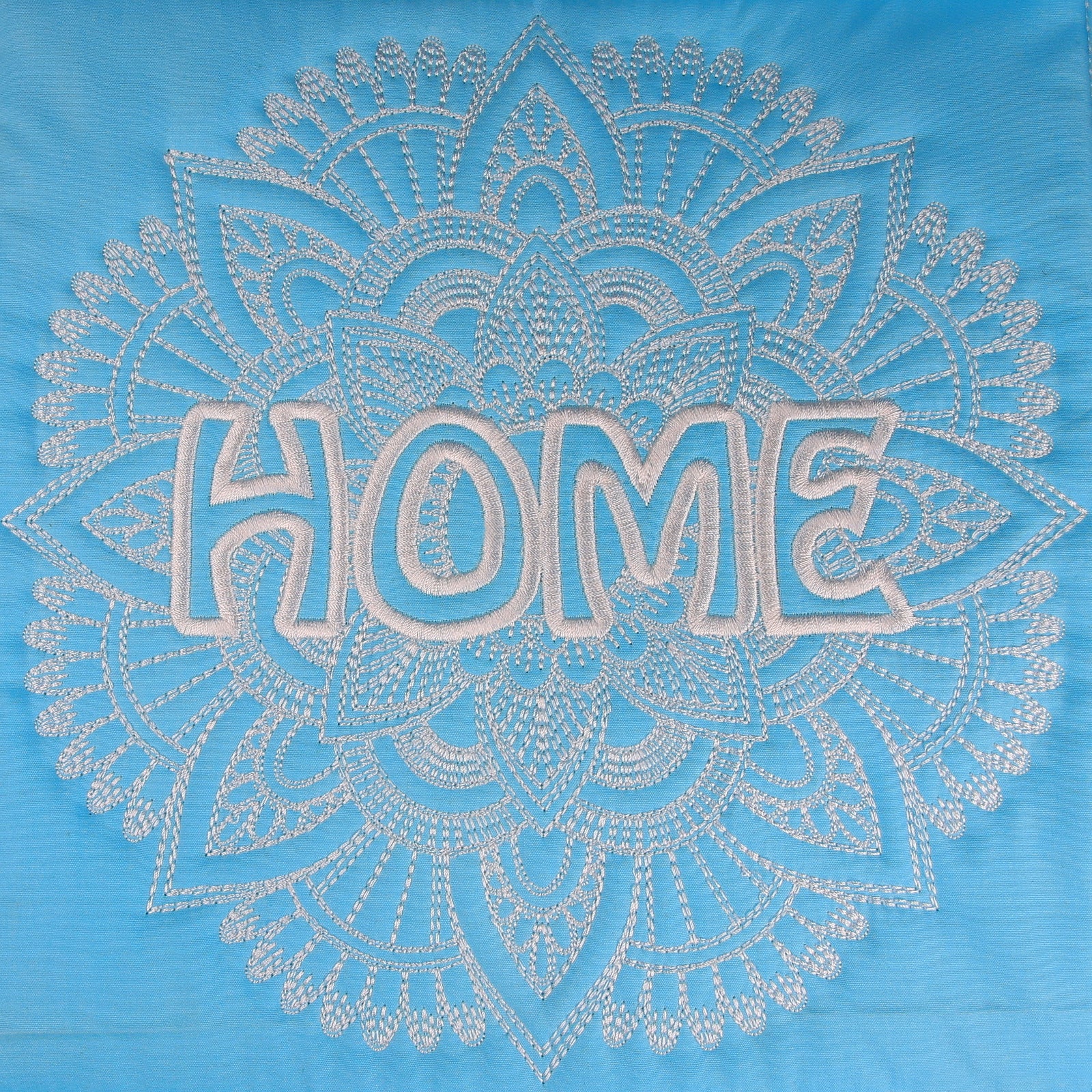 Blue tote bag with 'HOME' design hanging on a hook against a white wall.