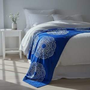 Blue mandala-patterned throw blanket on a bed with white bedding and pillows.