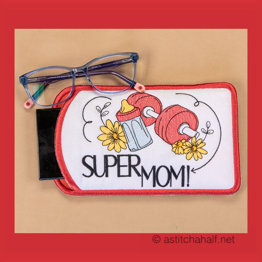 Eyeglass case with machine embroidery design featuring text 'SUPER WOMAN!' and floral patterns, displayed alongside a pair of eyeglasses.