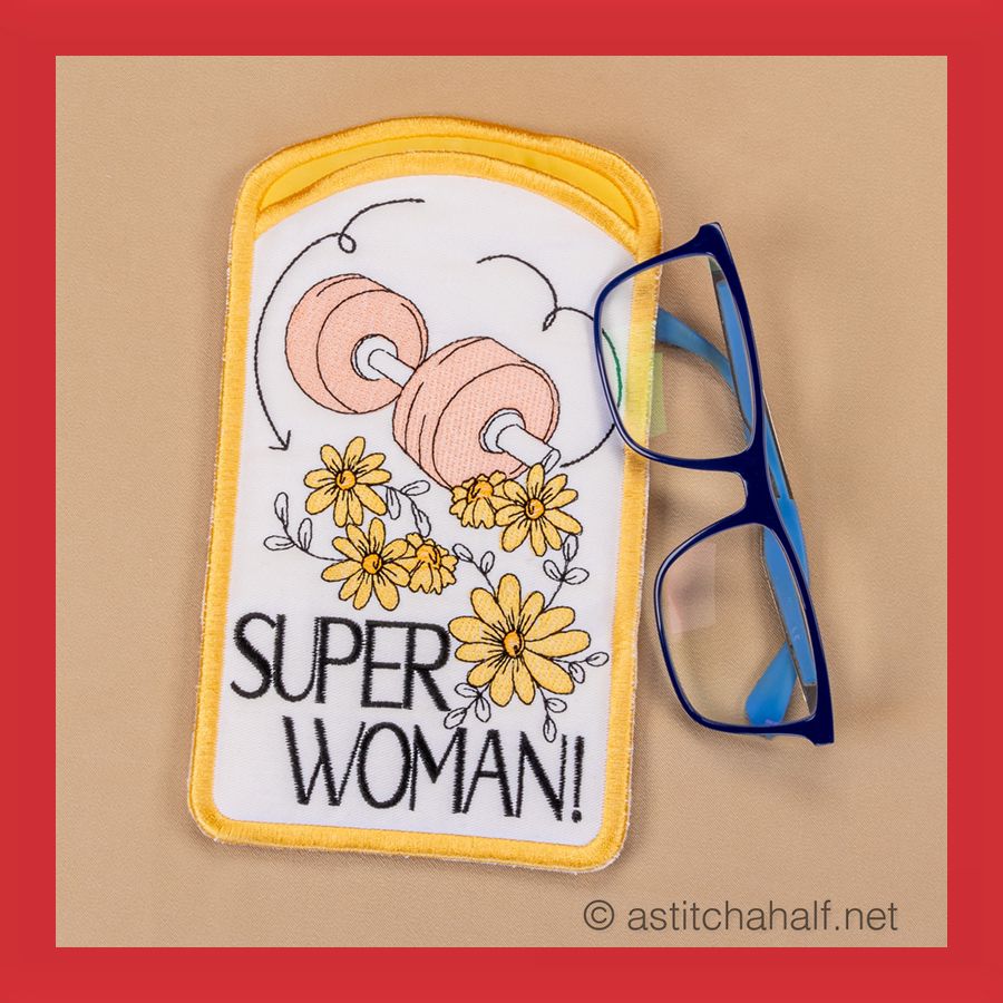 Eyeglass case with machine embroidery design featuring text 'SUPER WOMAN!' and floral patterns, displayed alongside a pair of eyeglasses.