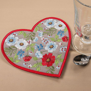 Heart-shaped embroidered coaster with floral design on a beige surface