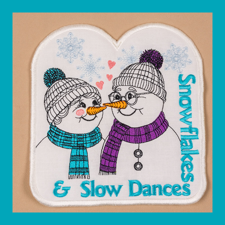 A mug rug with a design of two snowmen wearing hats and scarves, with hearts in the background and the text 'Snowflakes & Slow Dances'.