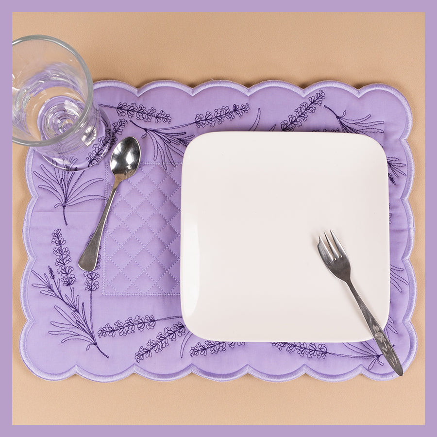 A purple placemat with an embroidered floral design, likely intended for use with a hoop machine for crafting.