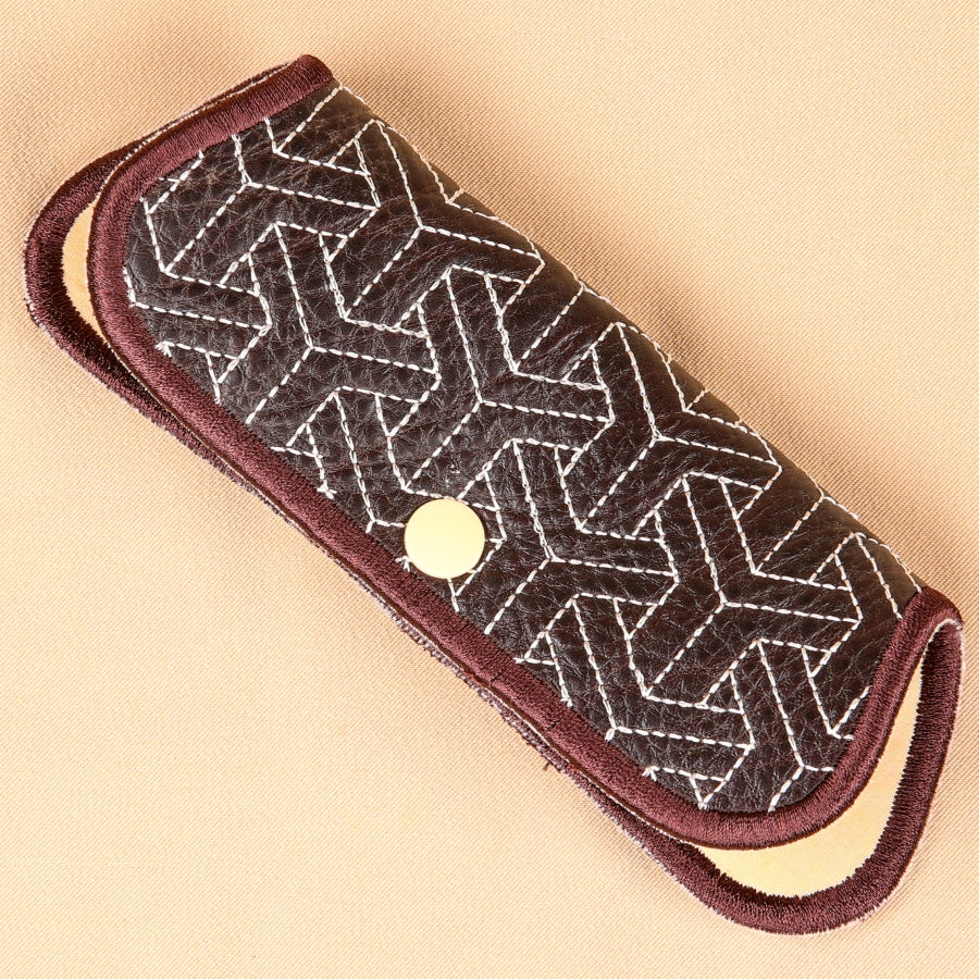 A hand holding an embroidered eyeglass sleeve with a geometric pattern.