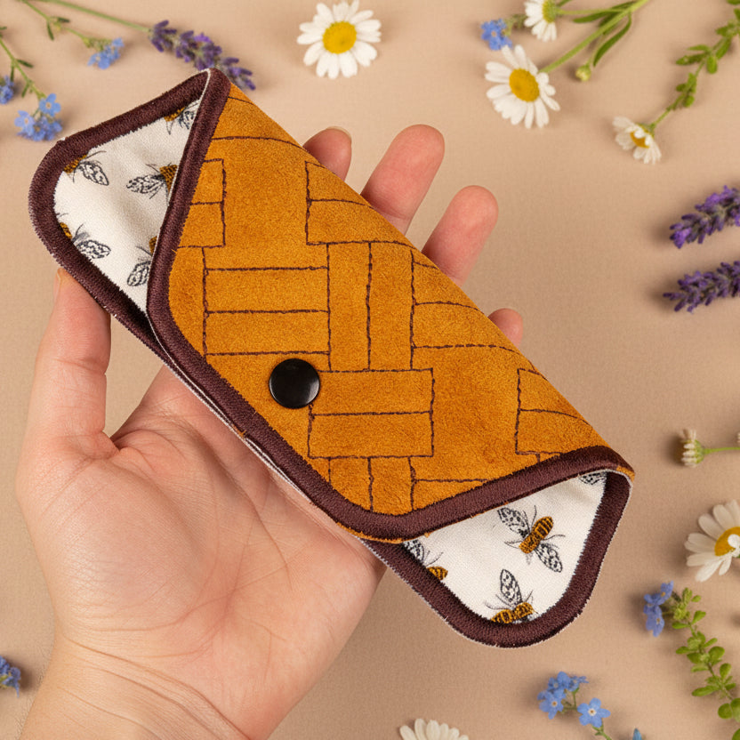 A hand holding an eyeglass sleeve with a geometric pattern, featuring a snap closure.
