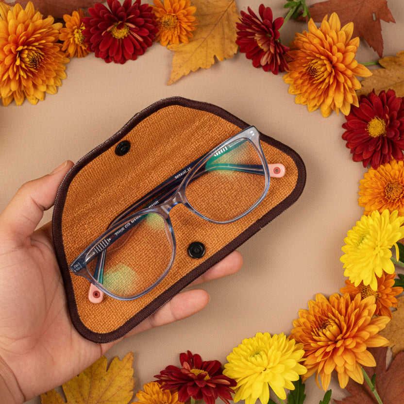 A hand holding a brown eyeglass sleeve with a geometric pattern. The sleeve is designed to hold glasses and has a lens cleaner built into the lining.