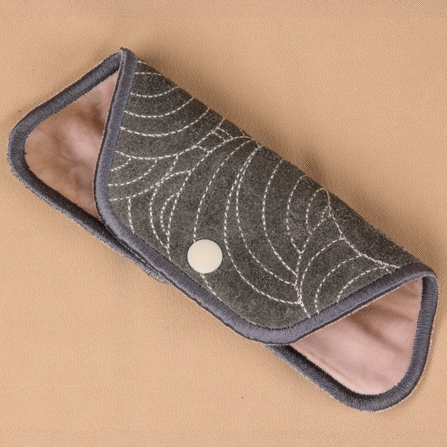 A hand holding a gray eyeglass sleeve with a leaf pattern and a blue elastic band.