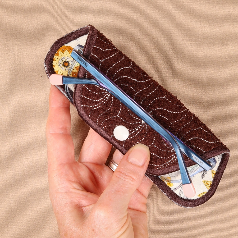 A hand holding a brown eyeglass sleeve with a patterned interior lining.