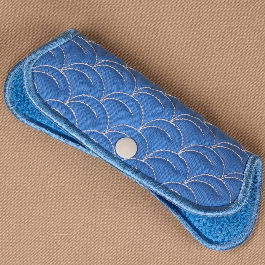 A hand holding a blue eyeglass sleeve with a geometric pattern.