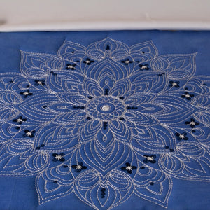 Blue fabric with intricate white embroidery and beadwork on a white background