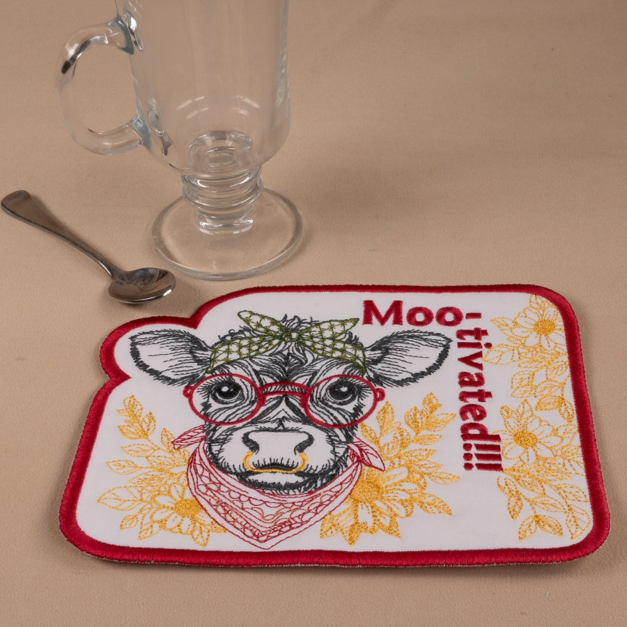 Coaster with cow illustration and 'Moo-tivated!!!' text on a beige surface with a glass and spoon.