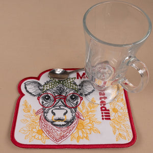 Coaster with cow design and spoon, glass mug on a beige background