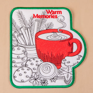 Patch with a red cup of coffee, cookies, and cinnamon sticks on a beige background with 'Warm Memories' text.