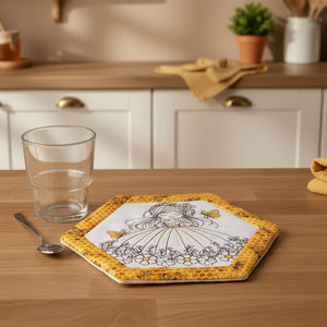 Hexagonal coaster with a design of a girl in a dress surrounded by butterflies and flowers, placed on a beige surface with a glass and spoon.