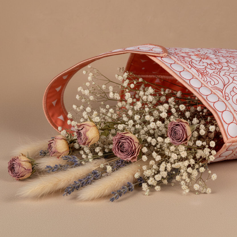 Decorative pink and white handbag with floral patterns on a beige surface.