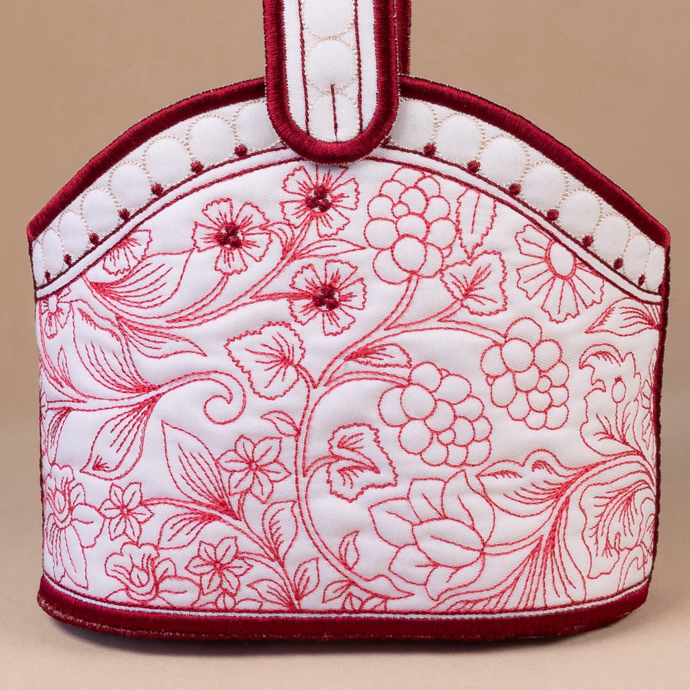 Handbag with floral pattern held by a hand, accompanied by flowers on a beige background