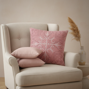 Beige armchair with pink patterned pillow and plain pillow, against a beige wall.