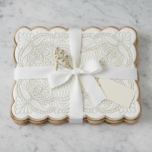 A stack of scalloped white cardstock gift boxes with embossed floral patterns, wrapped in a white ribbon with a bow and a blank tag, set on a light gray marble surface.