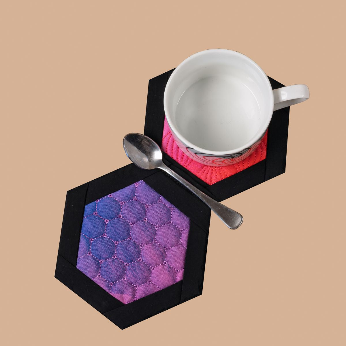 Hexagonal coasters with pink and blue design holding a white cup and saucer on a beige background