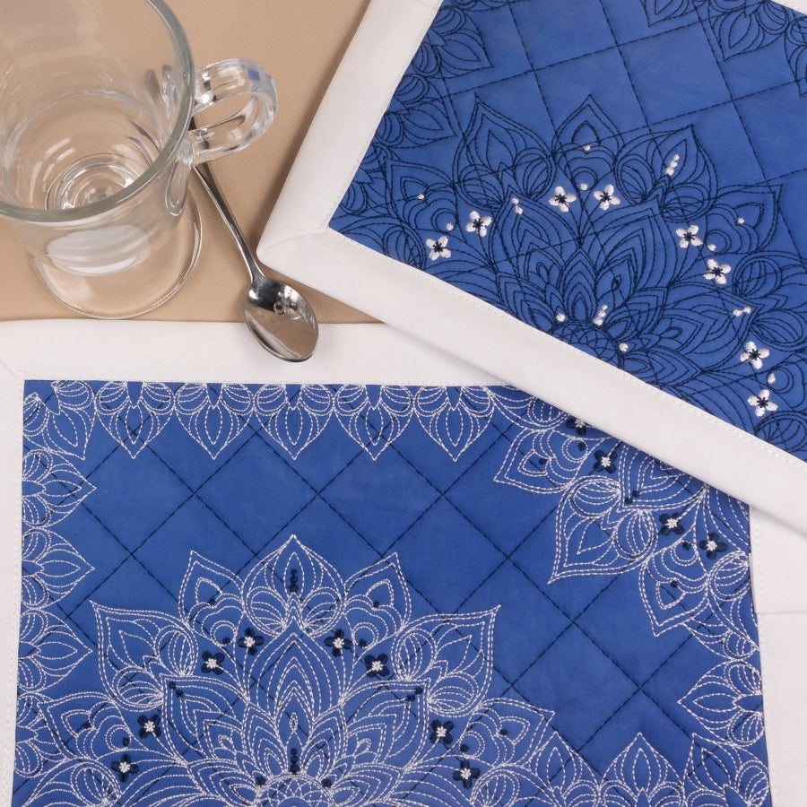 Blue placemats with white embroidery and bead details on a table setting.